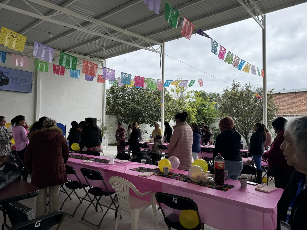 Personas conviven en una larga mesa rosa bajo un techo decorado con papel picado.