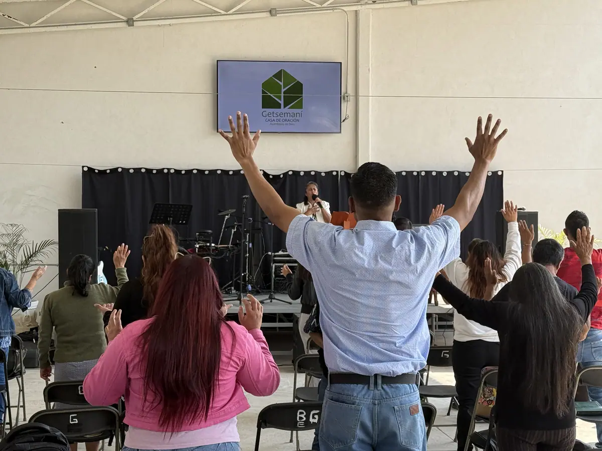 Personas con los brazos en alto, de espaldas, adoran frente al escenario donde una pantalla muestra el logo de Getsemaní.
